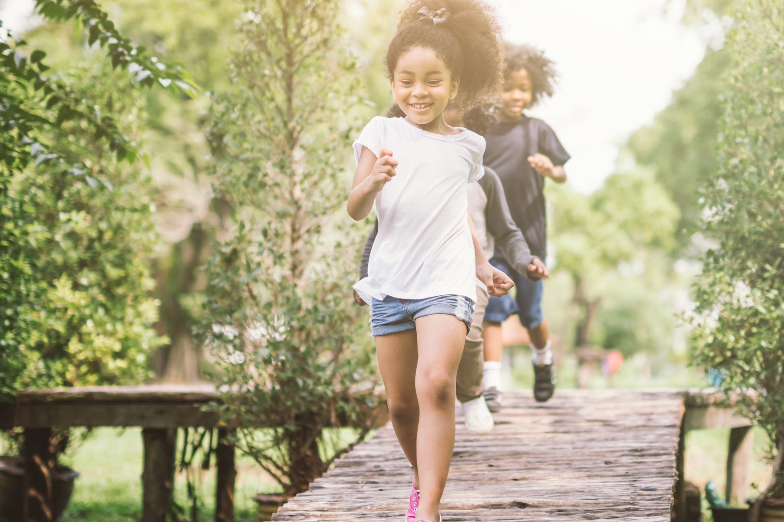 Young kids running on elevated trail surrounded by trees. They are smiling and having fun.